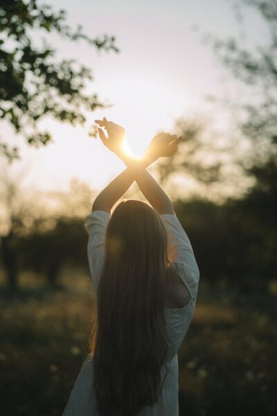 Young Woman Standing on the Meadow Stretching Her Arms Towards Rising Sun